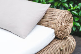 Outdoor wicker bed with white mattress and grey pillow. Clean place for relax and pleasure in hotel garden near pool