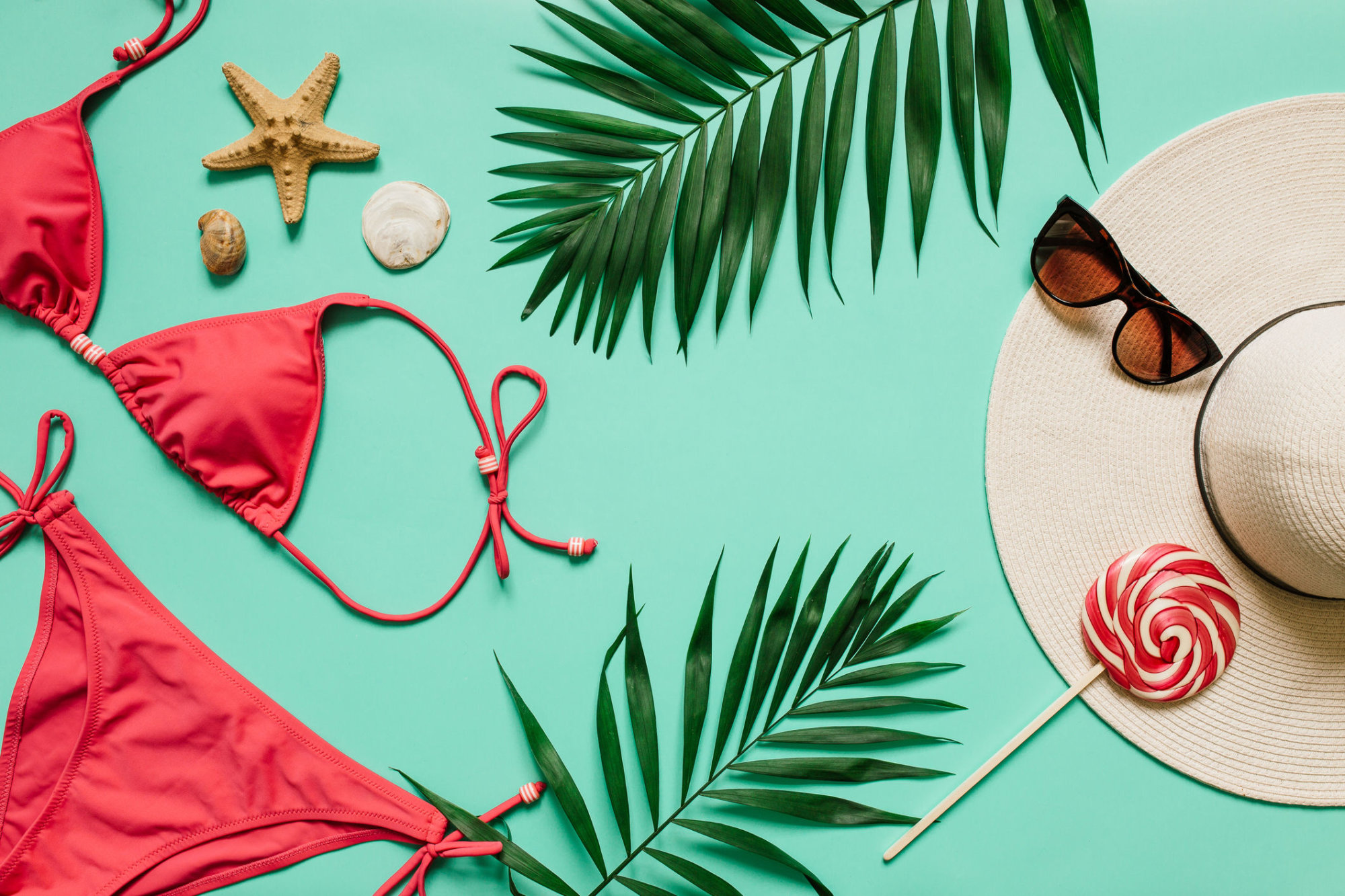 Red, pink bikini suit, lollipop, sunglasses, sea star on plain light cyan background. Empty space for copy, text, lettering. Summer vacation concept.