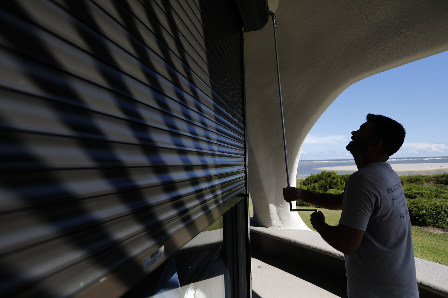 Chris Brace, from Charleston, S.C. lowers hurricane shutters on a client's house in preparation for Hurricane Florence at Sullivan's Island, S.C., Monday, Sept. 10, 2018. Brace said that after S.C. Gov. Henry McMaster ordered an evacuation the property owner asked for the house to be boarded up. (AP Photo/Mic Smith)