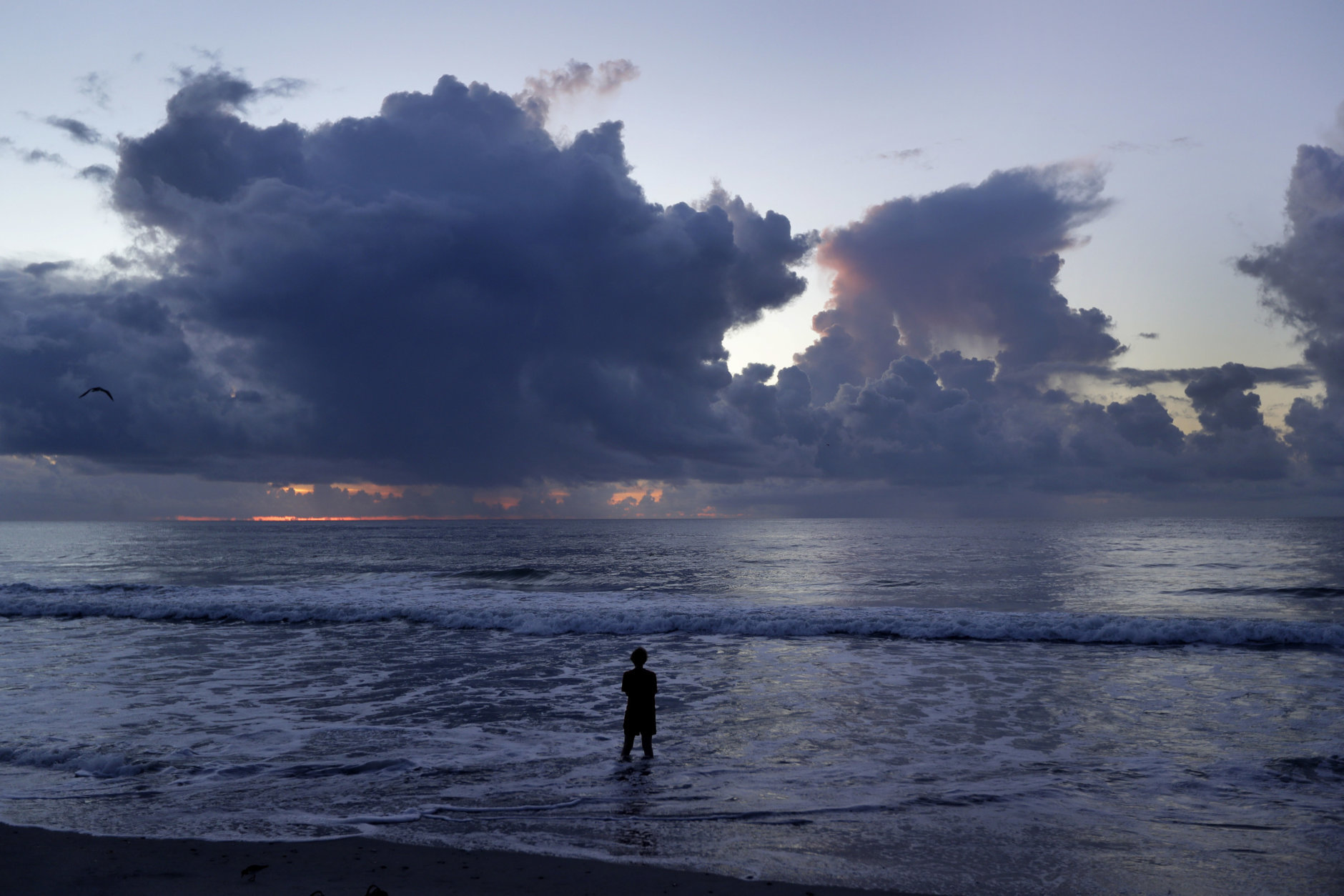 A woman stands in the surf and looks at the clouds at sunrise as Hurricane Florence approaches in Wrightsville Beach, N.C., Wednesday, Sept. 12, 2018. (AP Photo/Chuck Burton)