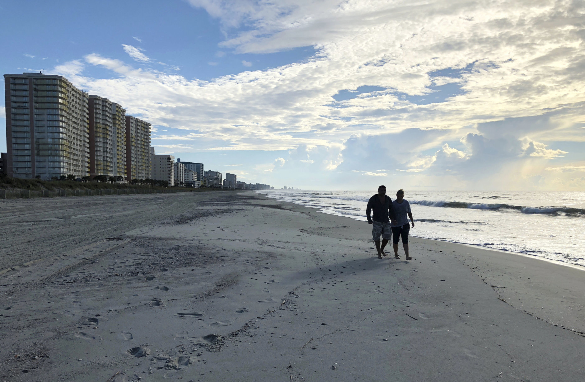 Chris and Nicole Roland walk down a beach in North Myrtle Beach, S.C. on Wednesday, Sept. 12, 2018. The couple boarded up their uncle's condominium and are leaving soon as Hurricane Florence approaches. (AP Photo/Jeffery Collins)