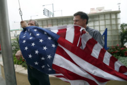Jim Mehlich, left, and Hans Seda, both with the Hilton Hotel, work to pull down an American flag in windy conditions, Thursday, Sept. 13, 2018, in Virginia Beach, Va., as Hurricane Florence moves towards the eastern shore. (AP Photo/Alex Brandon)