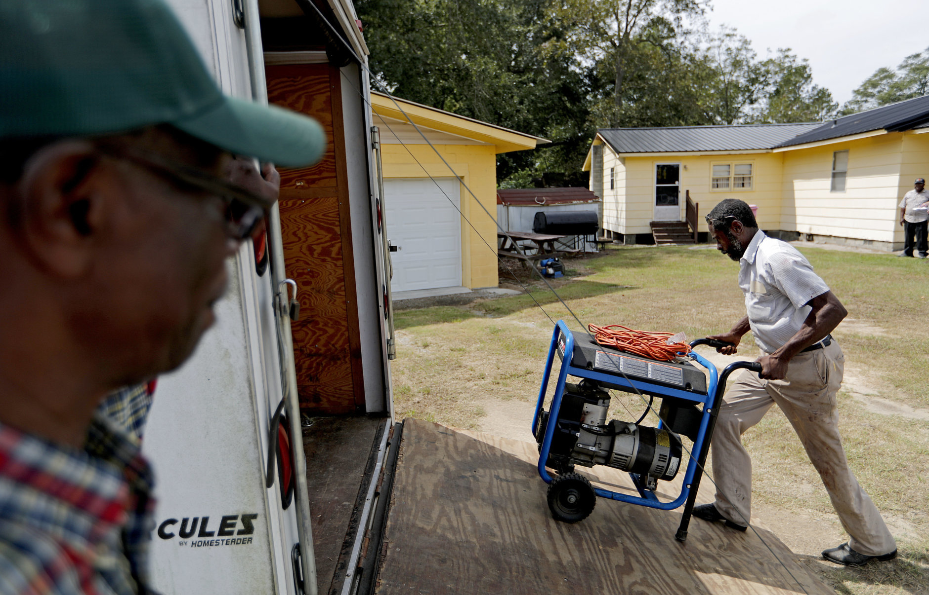 Stoney Williamson, right, unloads a generator for his brother-in-law, rear, whose home flooded two years ago from Hurricane Matthew, as Harry Campbell, left, looks on in Nichols, S.C., Thursday, Sept. 13, 2018, as Hurricane Florence approaches the east coast. (AP Photo/David Goldman)