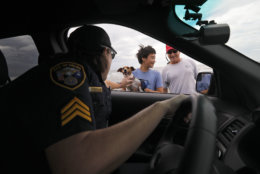 Isle of Palms police officer Detective Sergeant Sharon Baldrick speaks with Isle of Palms residents James Sireci, at right, and his son Aaron as she pets their family dog, Allie, on the Isle of Palms, S.C., as Hurricane Florence moves ashore near Wilmington, N.C., Friday, Sept. 14, 2018. (AP Photo/Mic Smith)
