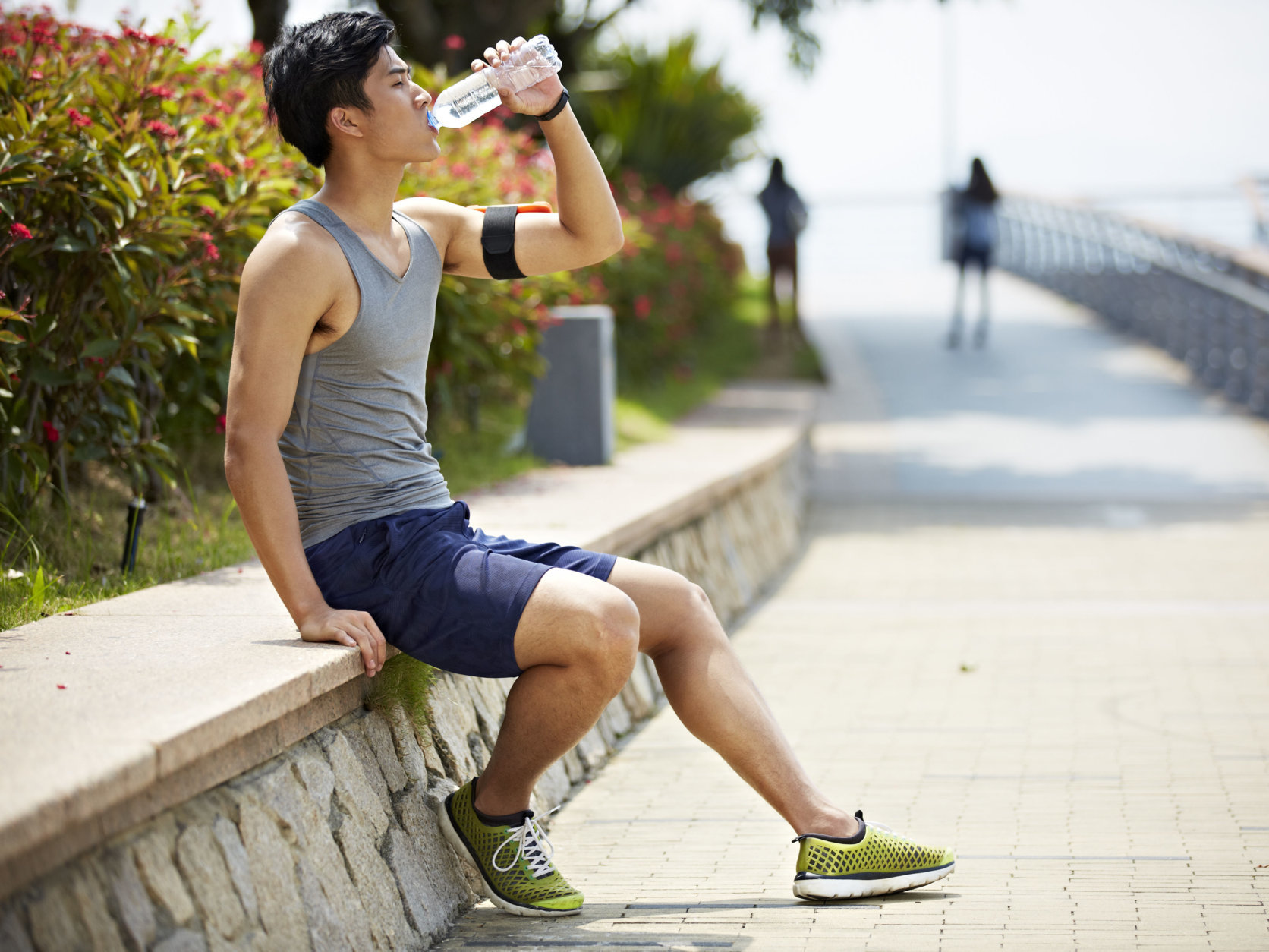 young handsome asian jogger taking a break and drinking water from a bottle, side view