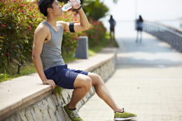 young handsome asian jogger taking a break and drinking water from a bottle, side view
