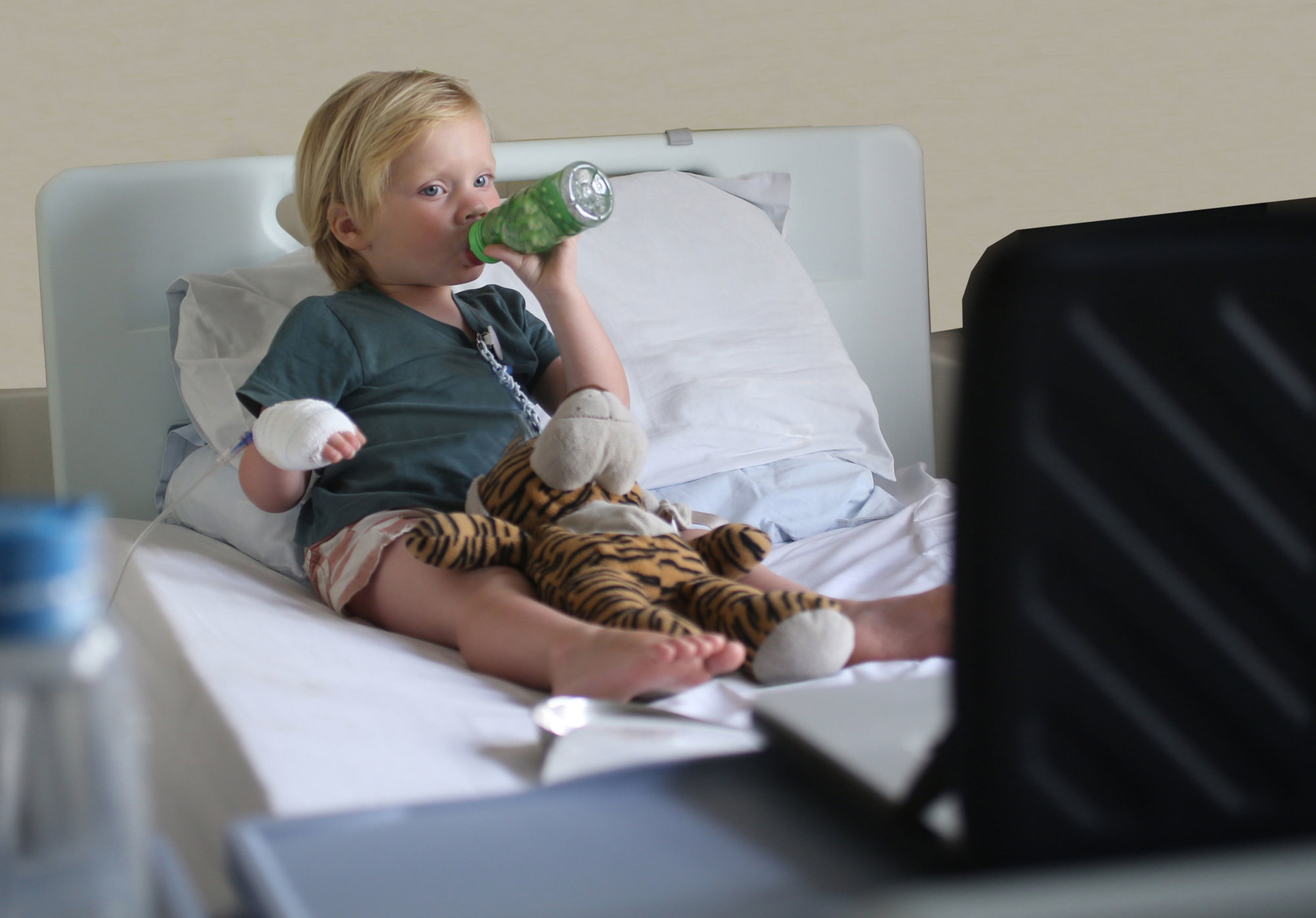 A boy in hospital drinking water while watching tv.