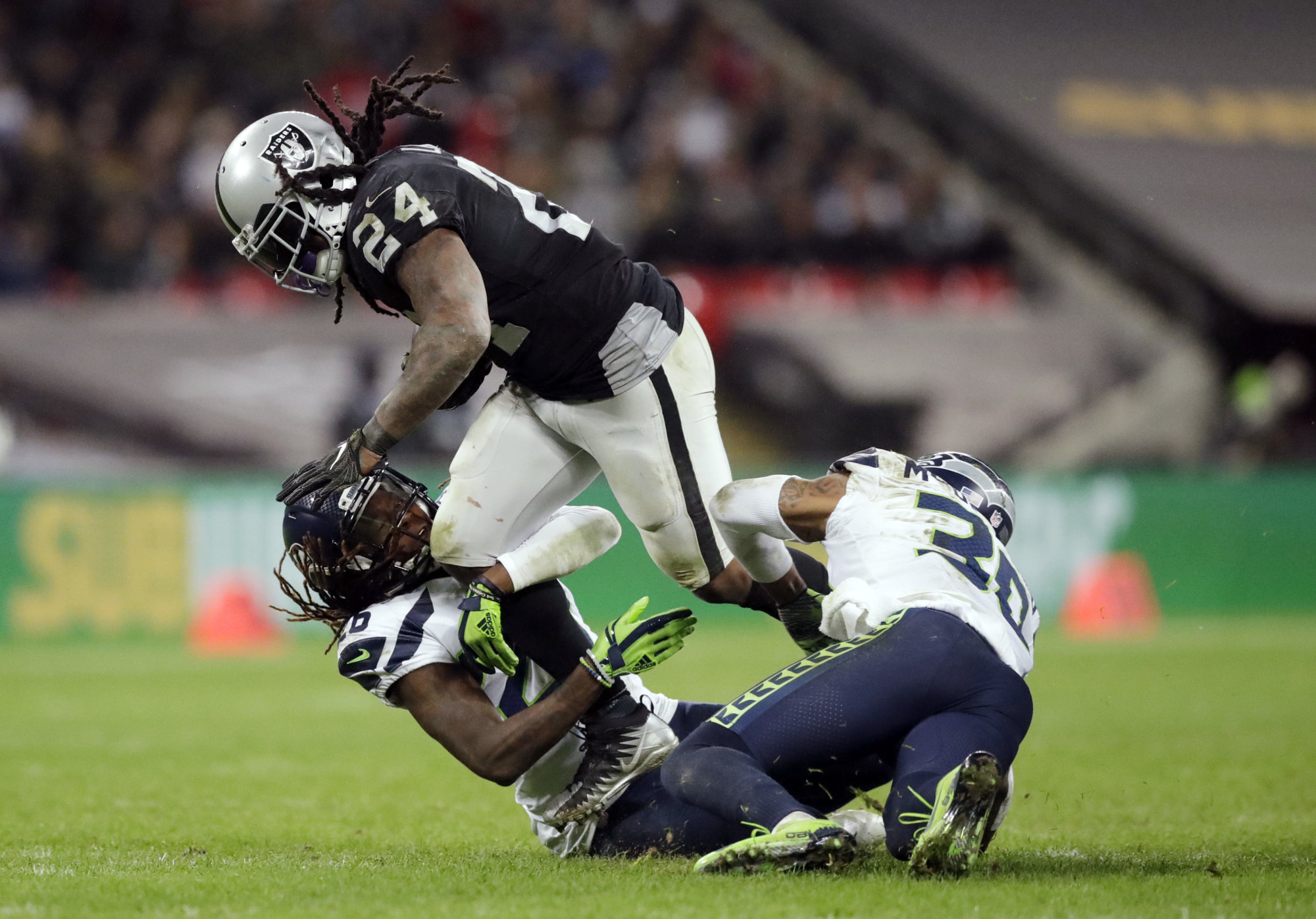 Oakland Raiders running back Marshawn Lynch (24) is tackled by Seattle Seahawks cornerback Shaquill Griffin (26) and strong safety Bradley McDougald (30) during the second half of an NFL football game at Wembley stadium in London, Sunday, Oct. 14, 2018. (AP Photo/Matt Dunham)