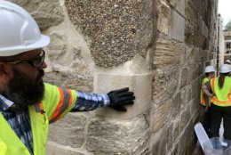 Construction manager Michael Lemaster takes a brief break while reporters are being briefed by park rangers. The dappled portion of the wall above his hand is an old concrete repair patch. He's touching a new stone that's part of the restoration project. Below Lemaster's hand is original stone from construction between the late 1820s and early 1830s. (WTOP/Kristi King)