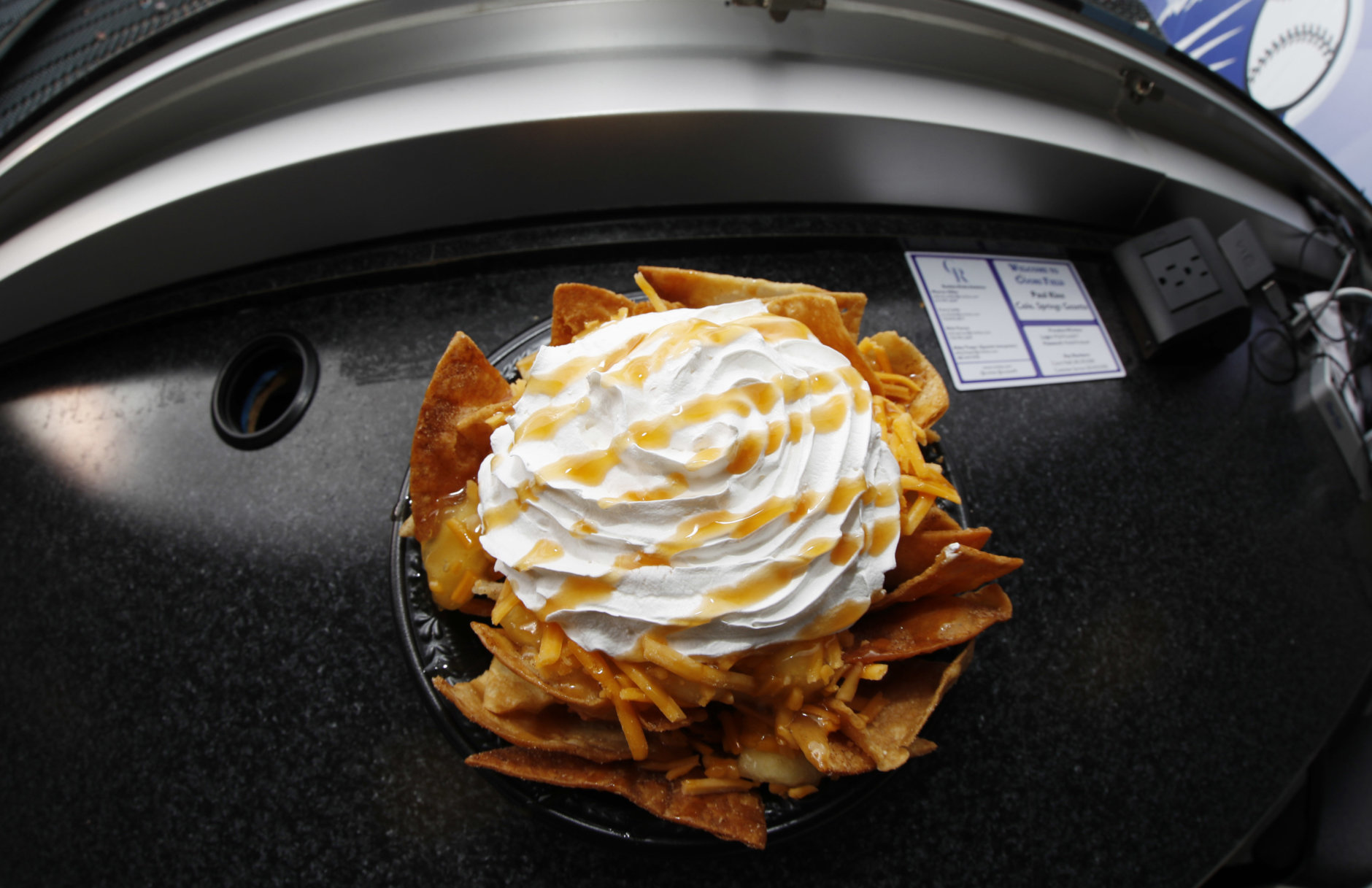 In this Saturday, May 6, 2017, a bowl of apple pie nachos is shown at Coors Field in Denver. The $6-bowl consists of cinnamon-covered nacho chips, apple pie filling, cheddar cheese, topped with whipped cream and then drizzled with caramel sauce. The concoction is rated at 740 calories. (AP Photo/David Zalubowski)