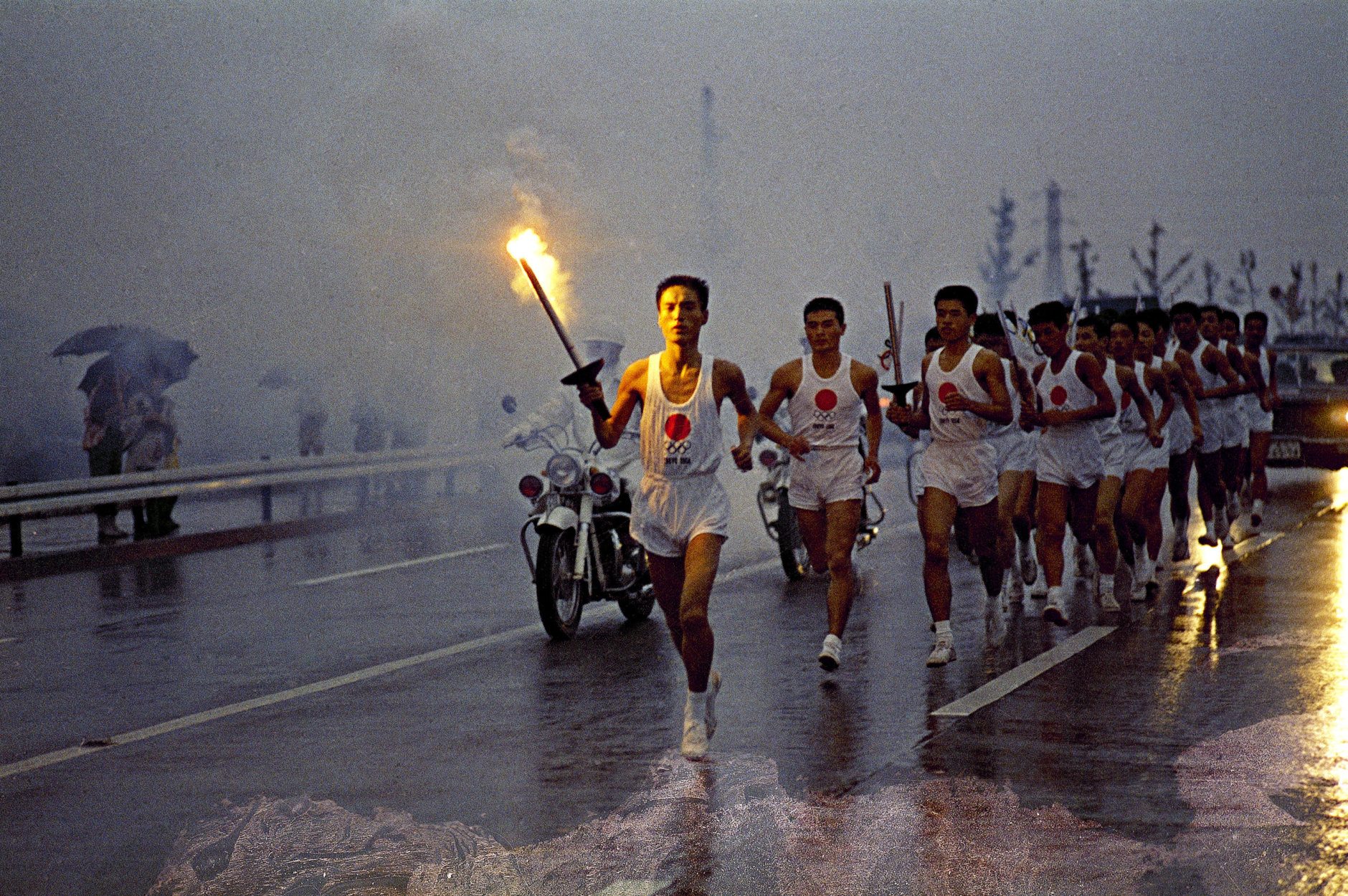 Japanese torchbearers of the Olympic flame relay team run through the rain on their way to the Olympic Stadium in October 1964 in Tokyo, Japan. The Olympic Flame is going to be lit by Yoshinori Sakai who was born in Hiroshima on August 6, 1945, the day the nuclear weapon destroyed that city. He symbolizes the rebirth of Japan after the Second World War when he opens the Summer Olympic Games on October 10, 1964 in Tokyo, Japan. (AP Photo)