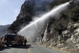Firefighters hose down hot spots from a wildfire along La Virgenes Rd. Monday, Nov. 12, 2018, in Calabasas, Calif. Los Angeles County Fire Chief Daryl Osby says he expects further damage assessments to show that hundreds more homes have been lost on top of the 370 already counted as lost in Southern California's huge wildfires. (AP Photo/Marcio Jose Sanchez)