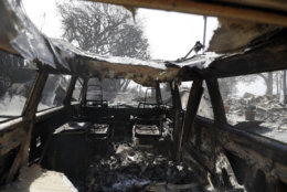 A wildfire-ravaged property is seen through the inside of a burned vehicle Monday, Nov. 12, 2018, in Malibu, Calif. Los Angeles County Fire Chief Daryl Osby says he expects further damage assessments to show that hundreds more homes have been lost on top of the 370 already counted as lost in Southern California's huge wildfires. (AP Photo/Marcio Jose Sanchez)