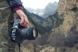 A female hand holds a camera against a caucasian mountain landscape