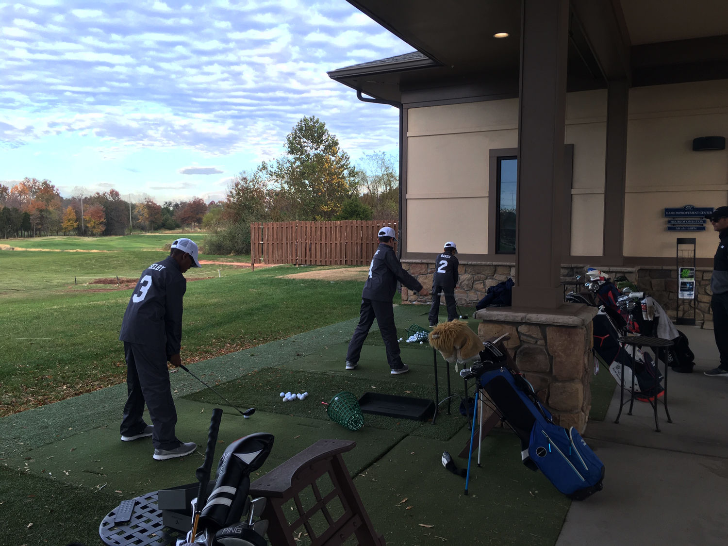 Coach Scott Holmes (right) watches as the team hits off the range. The 13 and under squad is in just its fifth year. (WTOP/Noah Frank)
