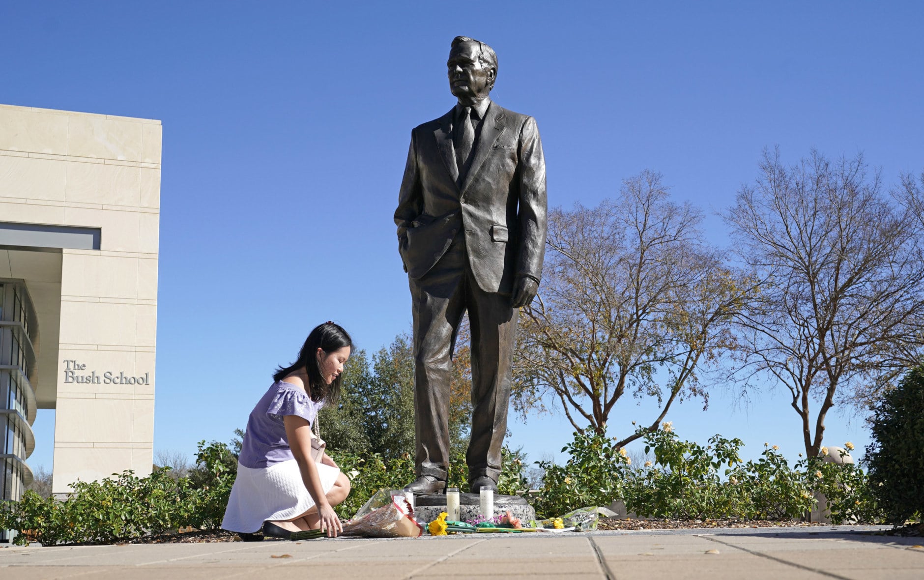 Thu Ton, of Dallas, places flowers at the base of a statue of former President George H.W. Bush outside the George H.W. Bush Presidential Library and Museum Saturday, Dec. 1, 2018, in College Station. Bush has died at age 94. Family spokesman Jim McGrath says Bush died shortly after 10 p.m. Friday, Nov. 30, 2018, about eight months after the death of his wife, Barbara Bush.(AP Photo/David J. Phillip)