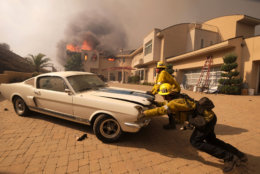 Firefighters push a car from a garage as a wildfire fire burns a home in Malibu, Calif., on Nov. 9, 2018. (AP Photo/Ringo H.W. Chiu)