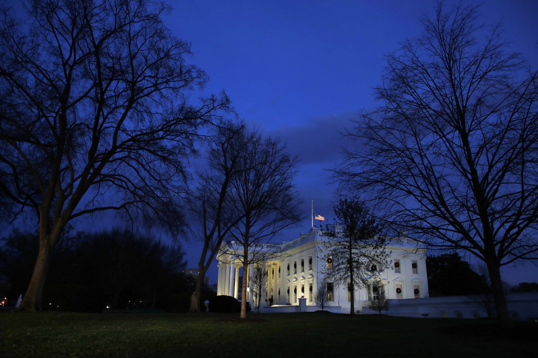 With the American flag at half-staff, dusk falls over the White House, Monday, Dec. 3, 2018, in Washington, as the state funeral for former President George H. W. Bush begins at the U.S. Capitol. (AP Photo/Jacquelyn Martin)