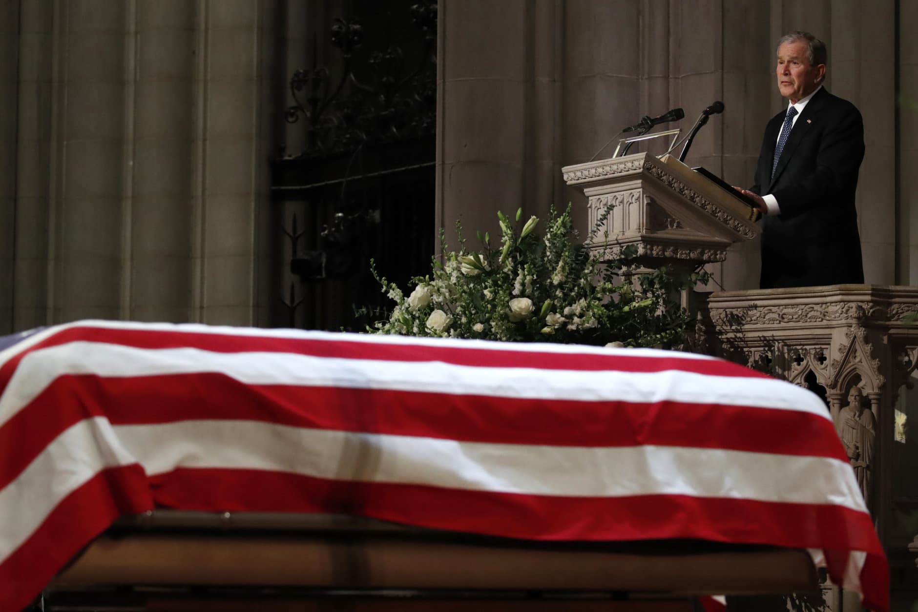 Former President George W. Bush speaks in front of the flag-draped casket of his father, former President George H.W. Bush, at the State Funeral at the National Cathedral, Wednesday, Dec. 5, 2018, in Washington. (AP Photo/Alex Brandon, Pool)