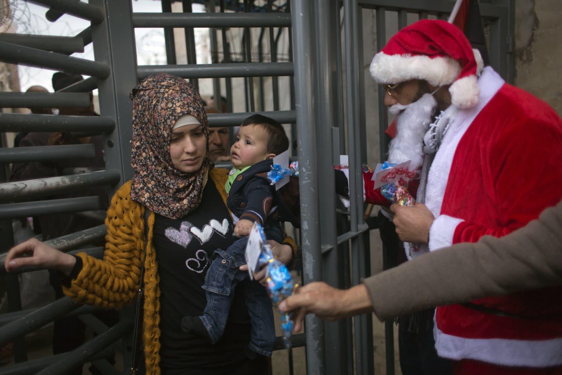 Palestinian protesters, some are dressed as Santa Claus, distribute sweets to people crossing through Israeli security gates during a protest in front of an Israeli checkpoint, in the West Bank city of Bethlehem, Sunday, Dec. 23, 2018. Christians around the world will celebrate Christmas on Monday. (AP Photo/Nasser Nasser)