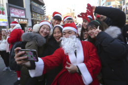Volunteers clad in Santa Claus costumes take a selfie as they gather to deliver gifts for the poor in downtown Seoul, South Korea, Monday, Dec. 24, 2018. (AP Photo/Ahn Young-joon)