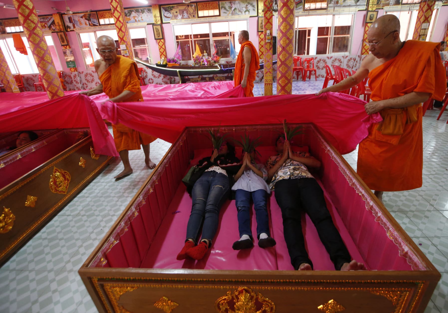 Monks cover worshippers lying in coffins at the Takien temple in suburban Bangkok, Thailand Monday, Dec. 31, 2018. Worshippers believe that the coffin ceremony – symbolizing death and rebirth – helps them rid themselves of bad luck and are born again for a fresh start in the new year. (AP Photo/Sakchai lalit)