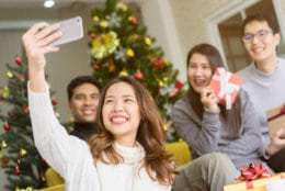 close up on christmas pine tree branch with decoration and group of diverse friends holing glass and cheers for celebrate in living room at home , xmas and happy new year party concept