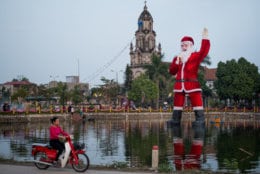 HANOI, VIETNAM - DECEMBER 23: A giant, floating Santa Claus stands in the lake in front of Phu My Cathedral on December 23, 2018 outside Hanoi, Vietnam. In Vietnam, a predominantly Buddhist nation, Christmas is not an official public holiday, but many people have adopted it as both a religious festival and a new cultural tradition. (Photo by Linh Pham/Getty Images)