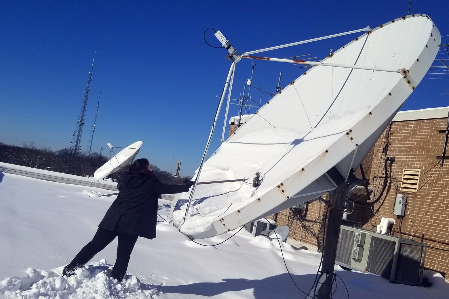 WTOP's Lisa Weiner clears the station satellite dish of snow. (WTOP/Jared Ruderman)