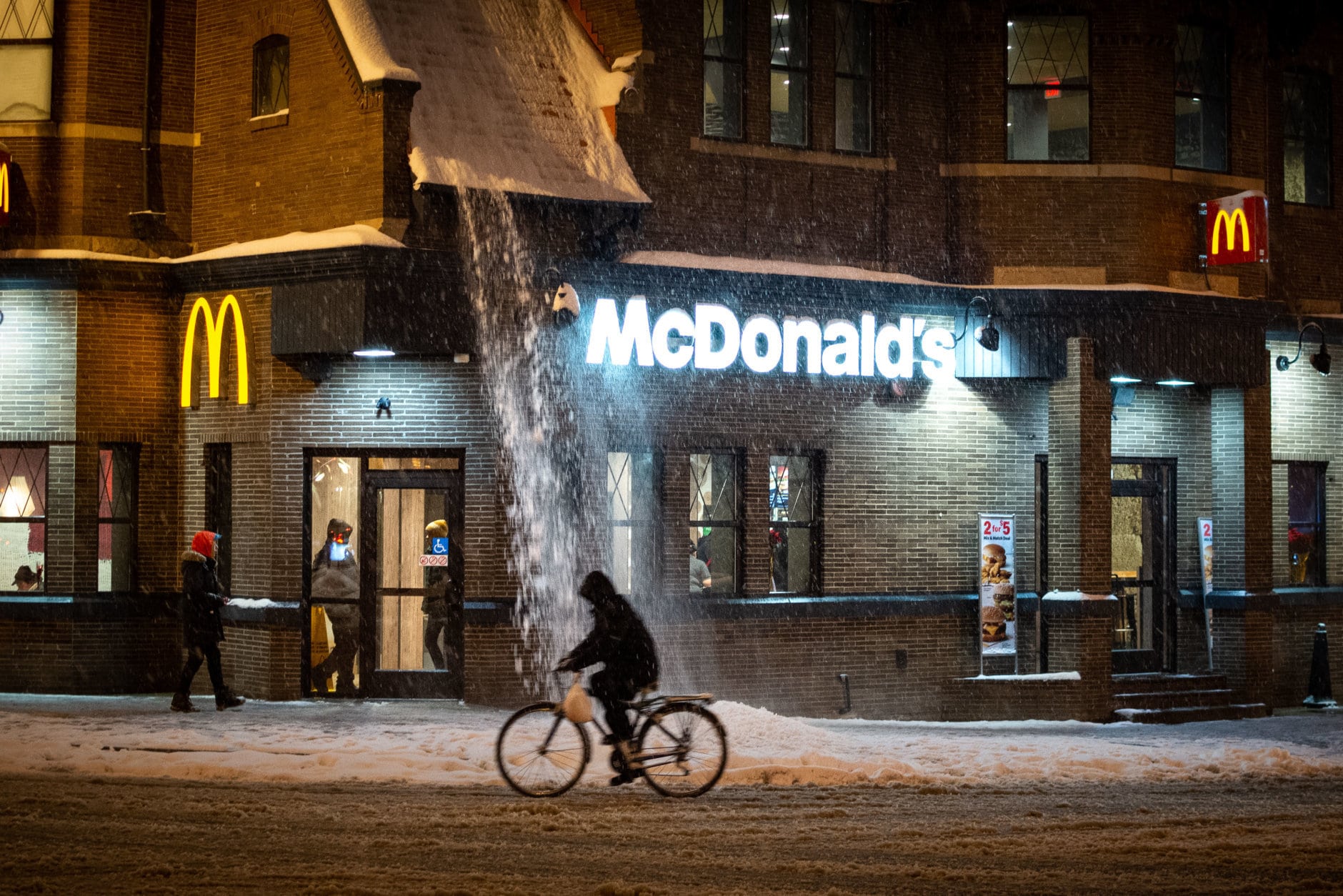Snow drifts down from the roof of a McDonald's restaurant in Adams Morgan. Despite the slush, life in one of the D.C.'s most popular neighborhoods went on largely as normal on Sunday night, with most bars and stores still open. (WTOP/Alejandro Alvarez)