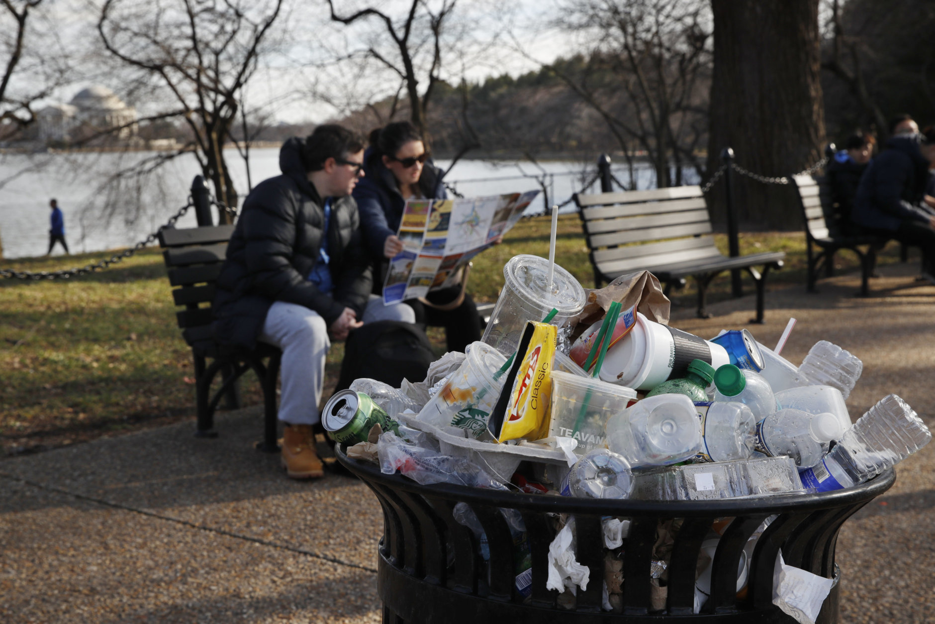 A trash can overflows as people site outside of the Martin Luther King Jr. Memorial by the Tidal Basin, Thursday, Dec. 27, 2018, in Washington, during a partial government shutdown. Chances look slim for ending the partial government shutdown any time soon. Lawmakers are away from Washington for the holidays and have been told they will get 24 hours' notice before having to return for a vote. Washington area national parks will remain open during the partial government shutdown, but without visitor center services. (AP Photo/Jacquelyn Martin)