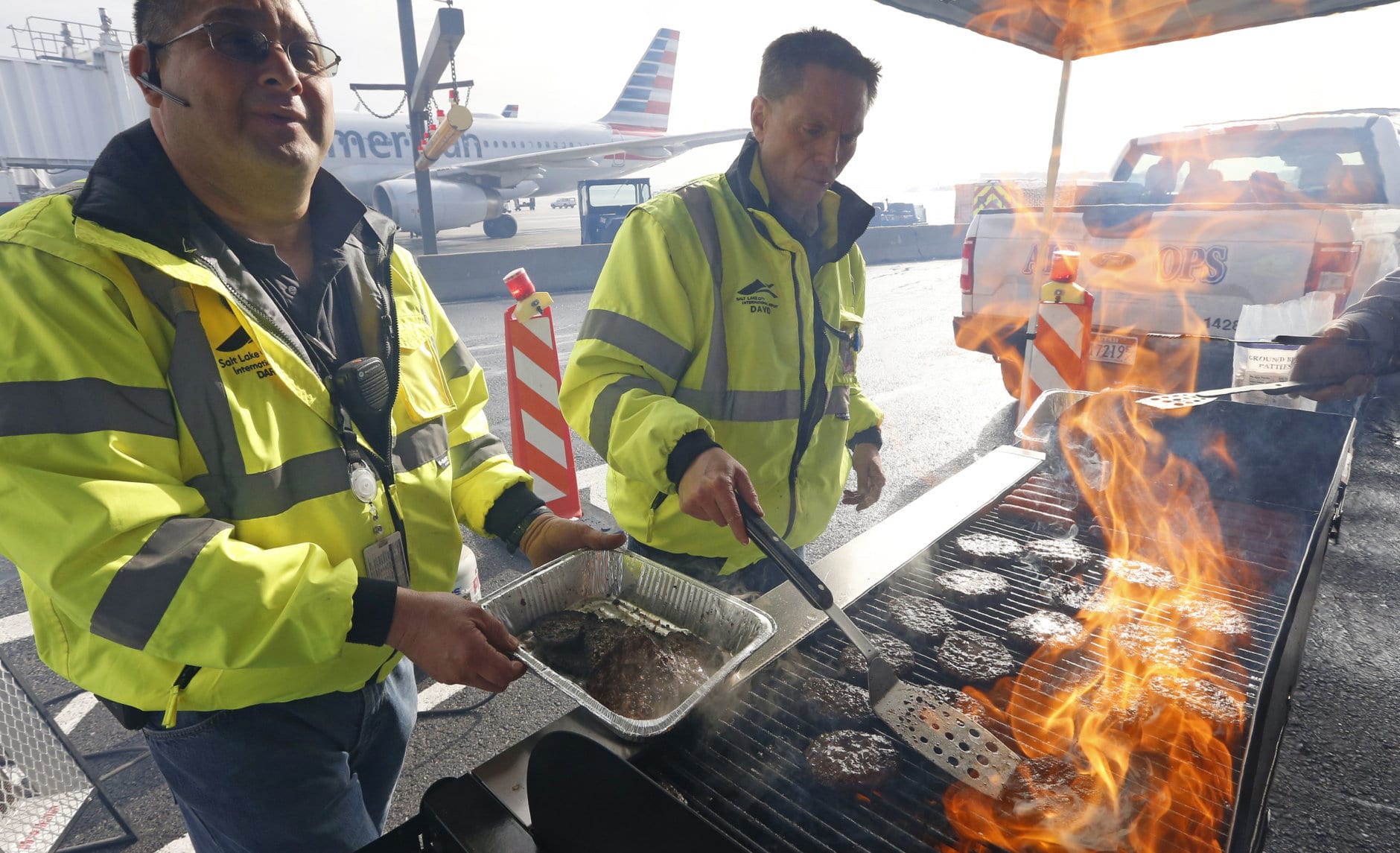 Airport operation workers wearing fluorescent safety jackets flipped burgers and hot dogs on a grill set up on a tarmac in front of a plane at Salt Lake City International Airport, Wednesday, Jan. 16, 2019, in Salt Lake City. In Salt Lake City, airport officials treated workers from the TSA, FAA and Customs and Border Protection to a free barbecue lunch as a gesture to keep their spirits up during a difficult time. (AP Photo/Rick Bowmer)