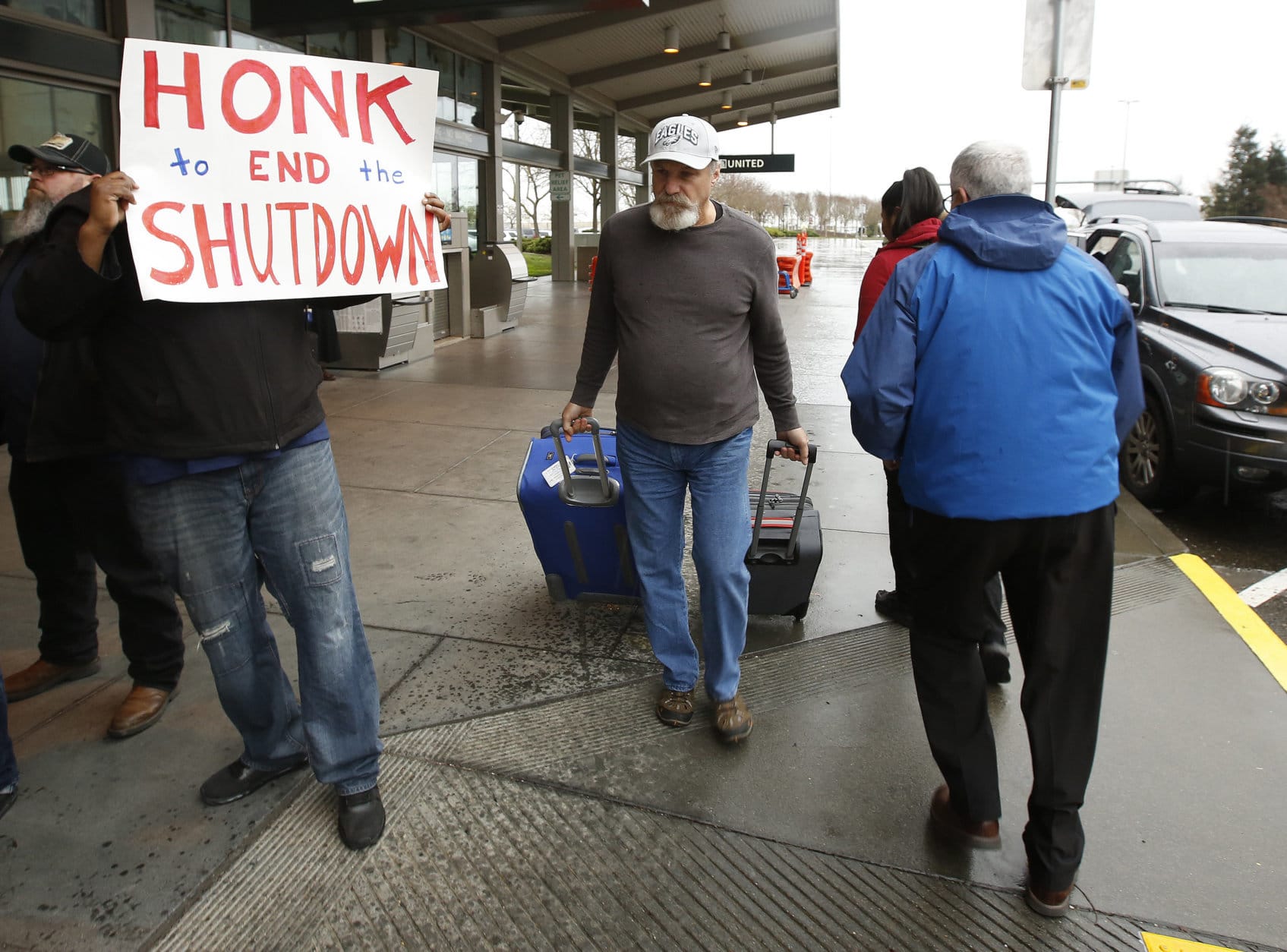 A man heading into the Sacramento International Airport passes demonstrators calling for President Donald Trump and Washington lawmakers to end the shutdown, Wednesday, Jan. 16, 2019, in Sacramento, Calif. More than two dozen federal employees and supporters called for an end to the partial government shutdown now in its fourth week. (AP Photo/Rich Pedroncelli)