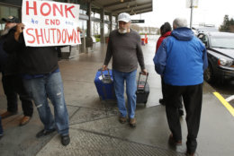A man heading into the Sacramento International Airport passes demonstrators calling for President Donald Trump and Washington lawmakers to end the shutdown, Wednesday, Jan. 16, 2019, in Sacramento, Calif. More than two dozen federal employees and supporters called for an end to the partial government shutdown now in its fourth week. (AP Photo/Rich Pedroncelli)