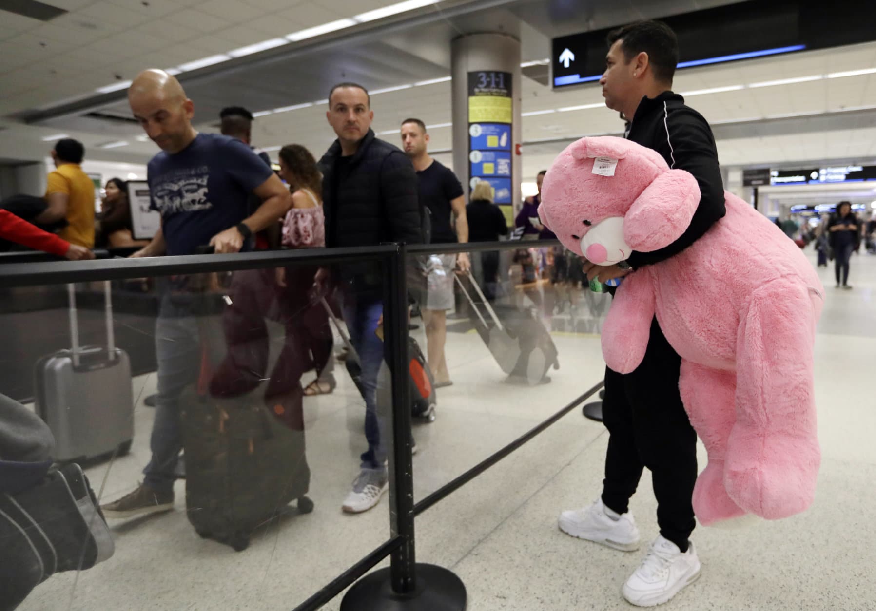 Carlos Gonzalez, right, watches as his daughter and other family members wait in line at a security checkpoint at Miami International Airport, Friday, Jan. 18, 2019, in Miami. The three-day holiday weekend is likely to bring bigger airport crowds. (AP Photo/Lynne Sladky)