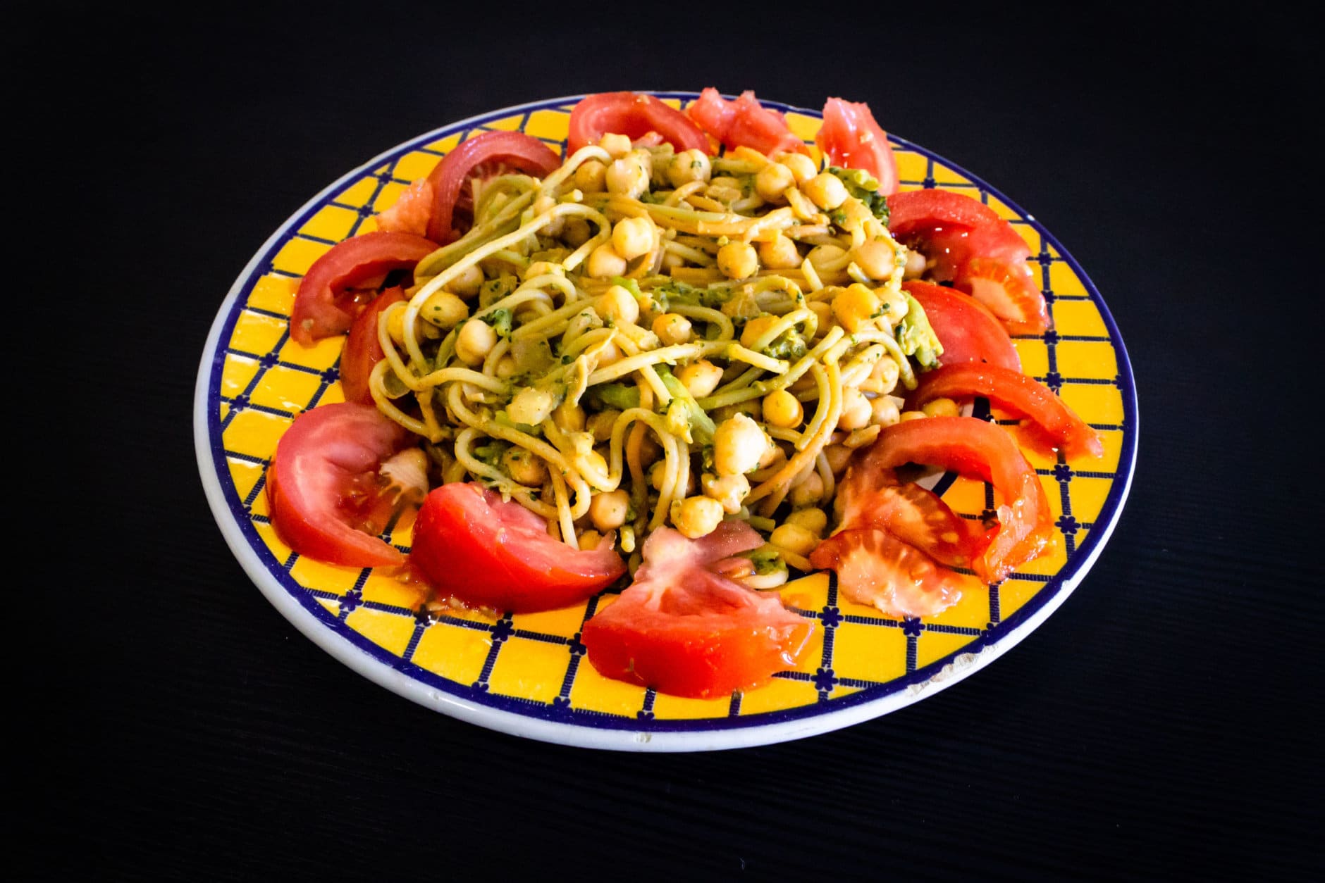 Food Dish on Black Wooden Background. Chickpeas, Spaghetti, Broccoli, Onions, Tomato. Yellow Blue Plate. Close Up.