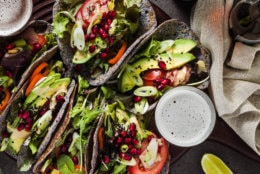 Gluten-free vegan tacos from black bean  with tomato and avocado salad  with tahini sauce and pomegranate seeds. healthy fast food for the whole family or party on a dark background with beer