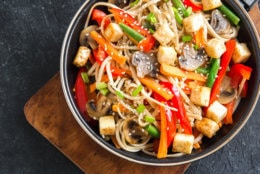 Stir fry with udon noodles, tofu, mushrooms and vegetables. Asian vegan vegetarian food, meal, stir fry in wok over black background, copy space.