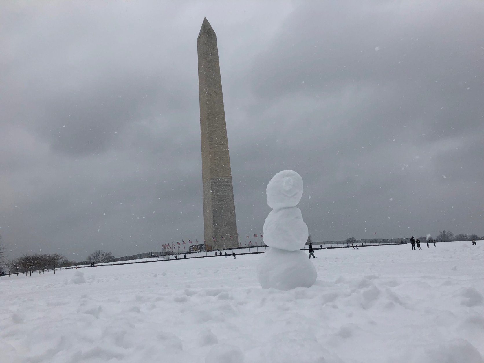 The Washington Monument towers over a snowman built on the National Mall. (WTOP/Keara Dowd)
