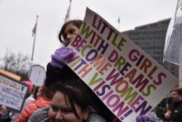 A young girl sits on her mother’s shoulders at Freedom Plaza following the march. (WTOP/Alejandro Alvarez)