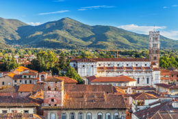 Vivid rooftops of city Lucca with background of colorful green mountains range, Italy.