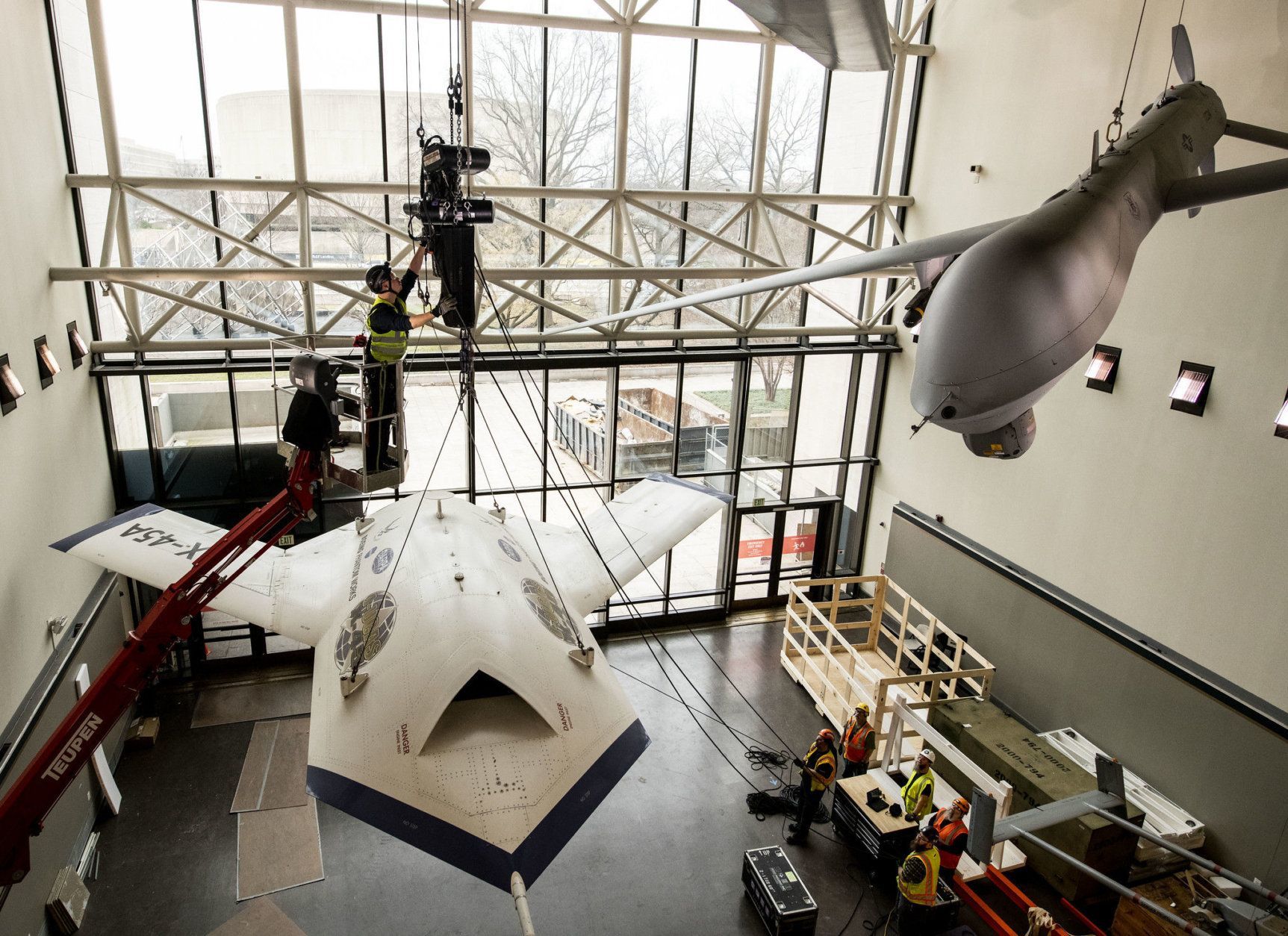 Contractors from iWeiss work to rig the X-45A drone for lowering in the Military Unmanned Aerial Vehicles (UAV) Gallery of the National Air and Space Museum in Washington, DC, February 22, 2019. (Smithsonian photo by Jim Preston)  Material is subject to Smithsonian Terms of Use. Should you wish to use National Air and Space material in any medium, please submit an Application for Permission to Reproduce NASM Material, available at:  https://airandspace.si.edu/permissions