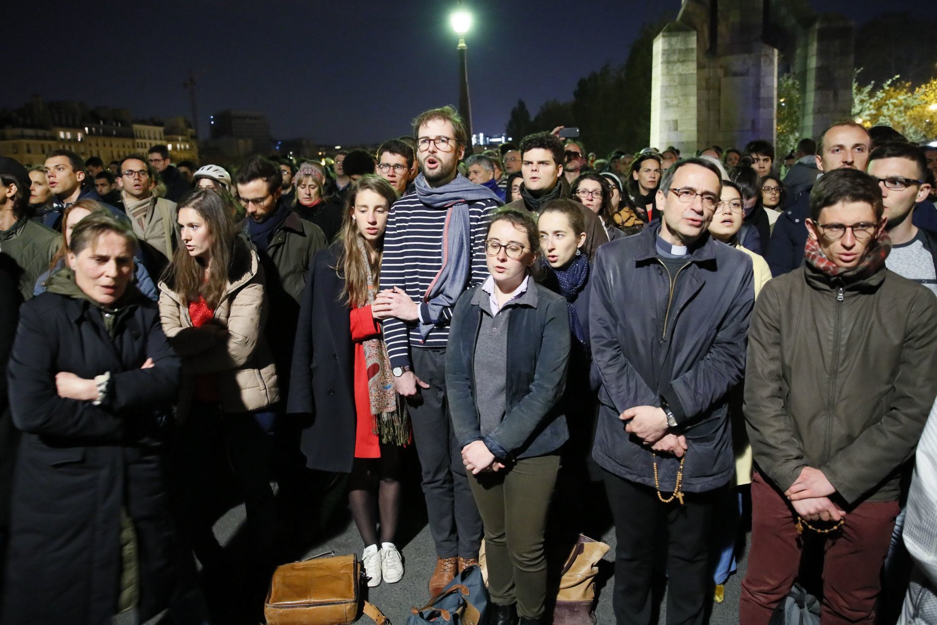 People pray as Notre Dame cathedral is burning in Paris, Monday, April 15, 2019. A catastrophic fire engulfed the upper reaches of Paris' soaring Notre Dame Cathedral as it was undergoing renovations Monday, threatening one of the greatest architectural treasures of the Western world as tourists and Parisians looked on aghast from the streets below. (AP Photo/Francois Mori)