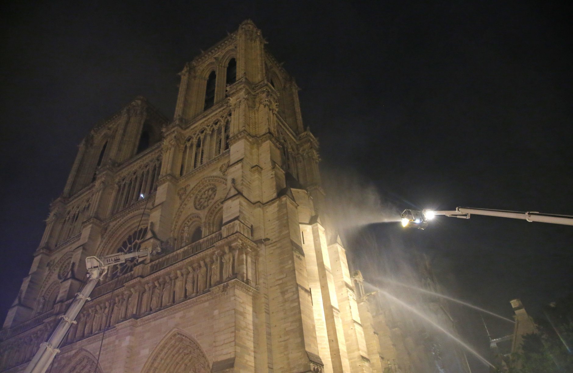 Firefighters spray water onto the facade of Notre Dame cathedral to stop the spread of a fire in Paris, Monday, April 15, 2019. Massive plumes of yellow brown smoke is filling the air above Notre Dame Cathedral and ash is falling on tourists and others around the island that marks the center of Paris. (AP Photo/Michel Euler)