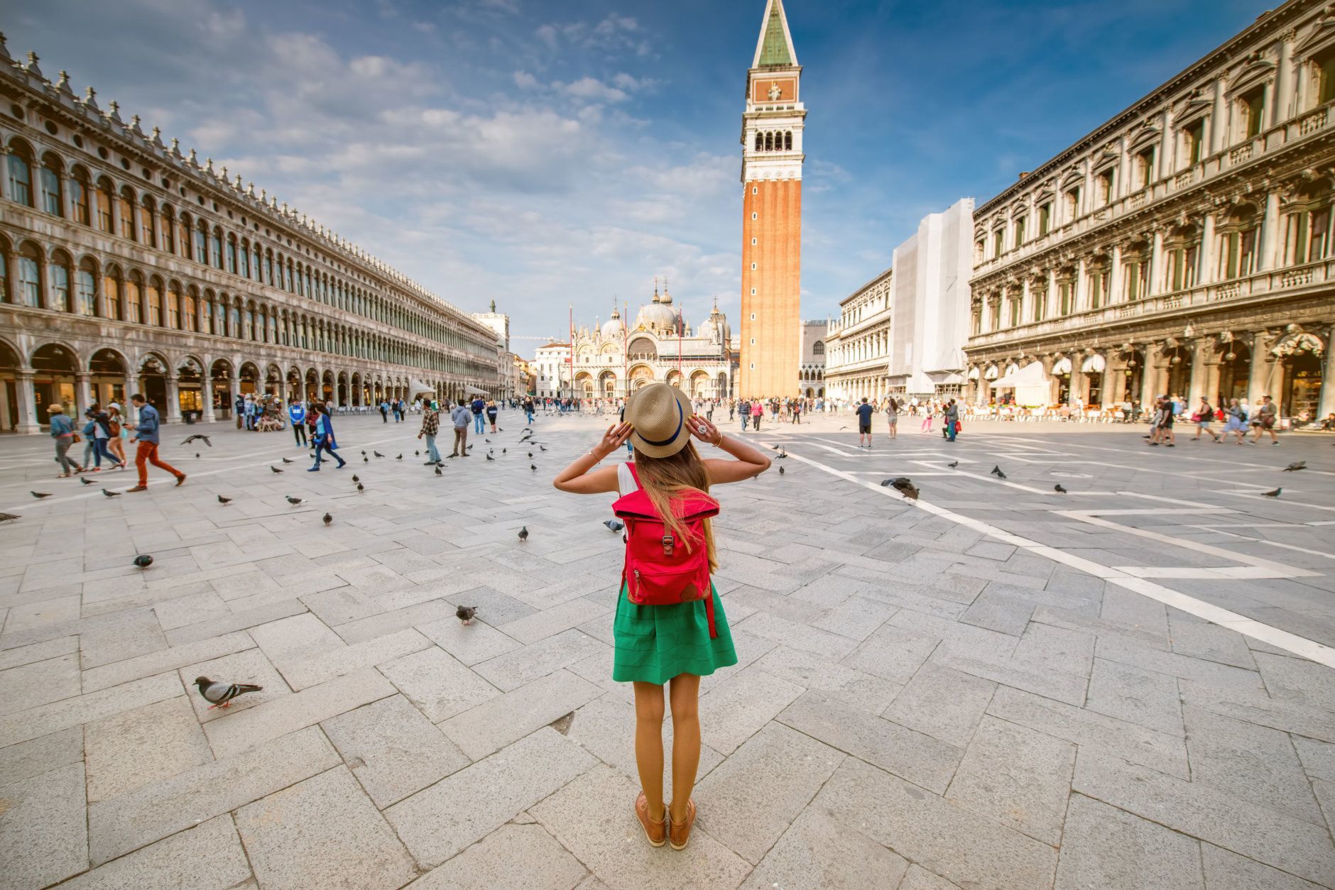 Jeune femme voyageuse avec chapeau et sac à dos debout sur la place San Marco avec tour et basilique en arrière-plan à Venise. Vue arrière avec copie espace