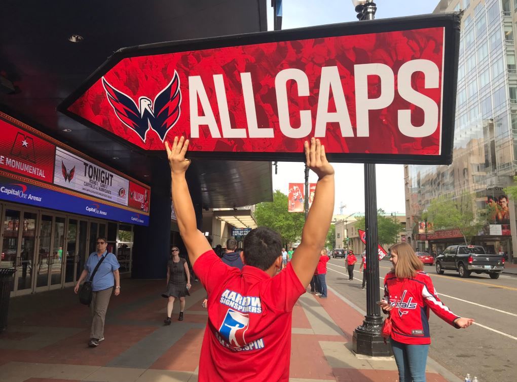 A sign spinner holds an All Caps sign during Game 7. (WTOP/Michelle Basch)