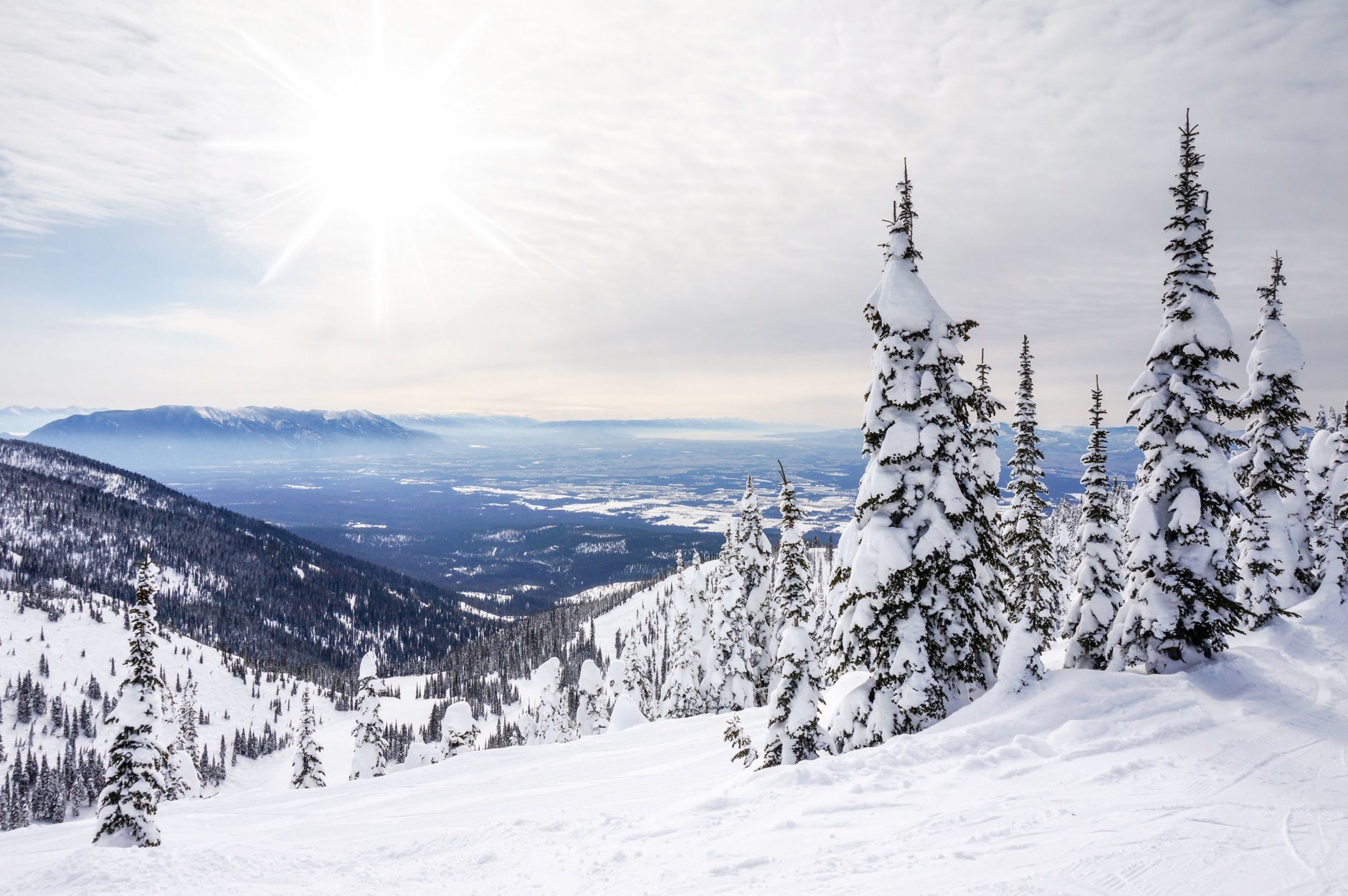 Paysage d'hiver blanc contre le soleil avec des nuages ​​duveteux à Whitefish, Montana, surplombant le parc national des Glaciers.