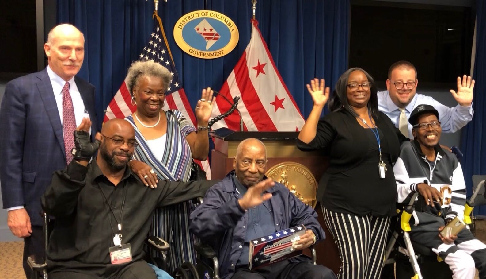 Leroy Tonic, middle, is surrounded by his family and members of the D.C. council on Friday, May 24, 2019. From left, D.C. Council Chair Phil Mendelson, Haleem Tonic, Bernadette Barnett, Leroy Tonic, Taenia Tonic, D.C. spokesman Josh Gibson and Leroy Milton Tonic Jr.(WTOP/Kristi King)