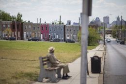 Row houses sit behind a man waiting at a bus stop, Sunday, May 3, 2015, in Baltimore. Gov. Larry Hogan has called for a statewide "Day Of Prayer And Peace" on Sunday after civil unrest rocked Baltimore. (AP Photo/David Goldman)