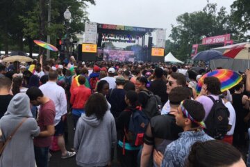 a crowd shields itself from the rain while gazing towards the stage at the Capital Pride Concert in 2019.